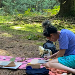 A woman sculpting clay at a creative art retreat in a green forest setting.