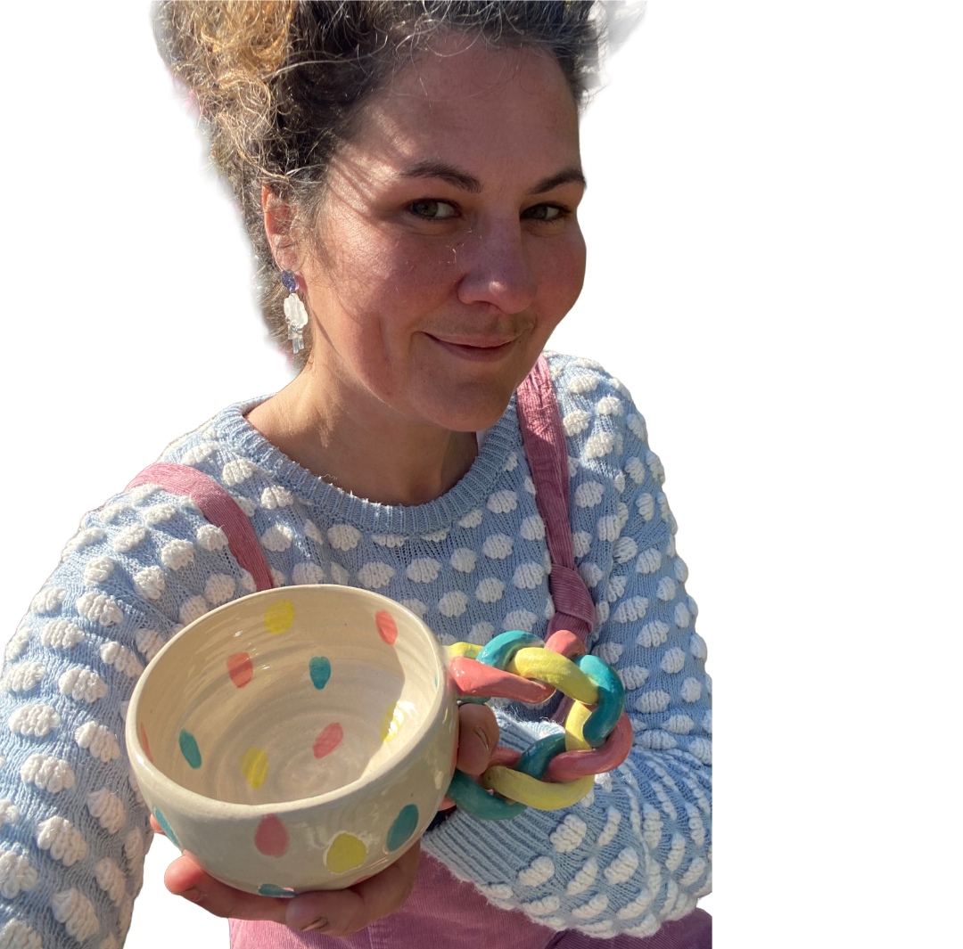 Ceramic artist Helen smiling while showcasing her handmade polka-dot pottery mug with a colourful braided clay handle.